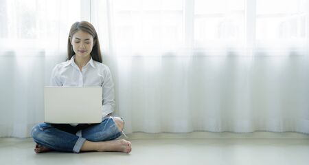 Asian women who are using a laptop in a warm house, a window with bright light. Work at home or home office, are encouraged to get a better job.の写真素材