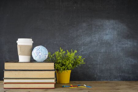 Education concept - books on the desk in the auditorium. School books, Coffee mugs, globe models on desk or back to school on black backgroundの写真素材