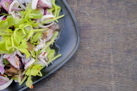 Fresh salad with seafood, tomatoes, celery and basil in a black bowl on rustic wooden background. Salad with squid, octopus, shrimp, mussel and black sesame seeds. Seafood concept. Top view.の写真素材