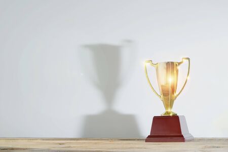 Celebrating the success that has happened, Gold trophy placed at work desk. There is a large reflection of the trophy. Free space to put text into advertising media.の写真素材
