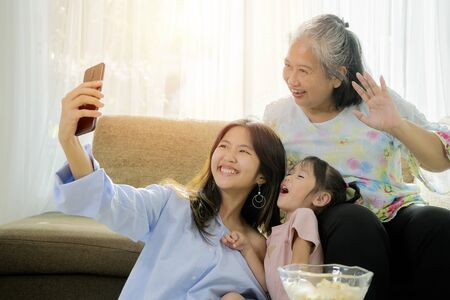 Granddaughter teaches Grandma using video calls, They use smartphones as communication devices. Everyone looks happy, smiling, cheerful. In the living room of his house.の写真素材