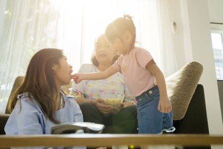 Different family relationships during the ages, grandmother, mother, grandchildren. There are activities together in the living room.の写真素材
