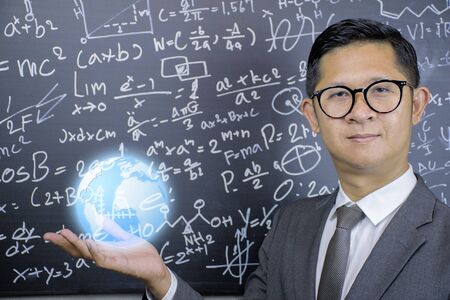 STEM concept.Mathematics teachers wear glasses, wear suits, look dignified, trustworthy.He opened his hand and had a globe on it.The background is a blackboard with mathematical formulas.の写真素材