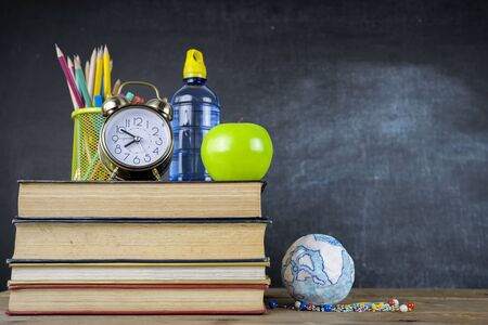 Back to school concept - books on the desk in the auditorium,Model globe, green apple, alarm clock. School books on desk or back to school on black background.の写真素材