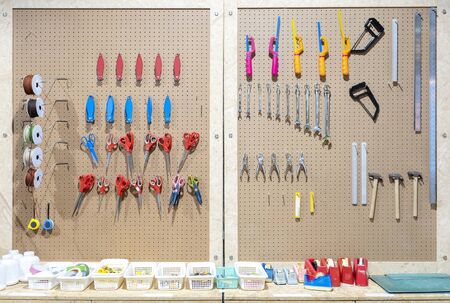 Workshop scene. Tools on the table and board. Glue, tape measure, steel ruler, screwdriver, wrench, scotch tape, yarn, scissors, hammer, cutter, orderly hanging, ready to use.の写真素材