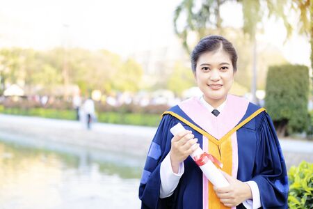 Cute Asian woman, she is successful in education. Happiness graduation day concept, woman graduate hand holding diploma.の写真素材