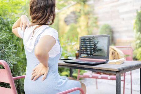 Young businesswoman feels uncomfortable sitting in office chair, woman massaging her back suffering from discomfort ache pain, incorrect posture from long sedentary work and lower backache conceptの写真素材
