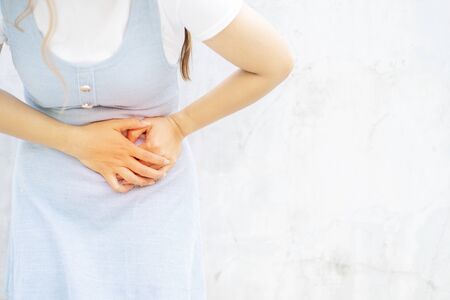 Woman in pain holding her stomach on the left side,  grey background, gastrointestinal tract diseasesの写真素材