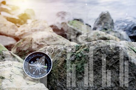 Business concepts, prospects for business, The compass is placed on the rocks in the hand and data is analyzed using stock market graphs on screen, financial data and technologyの写真素材
