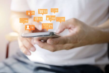 Close up of a man using mobile smart phone. Communication icons, messages, likes, notifications, using smart phones to monitor the work. typing text message at social network, sitting on sofa at homeの写真素材