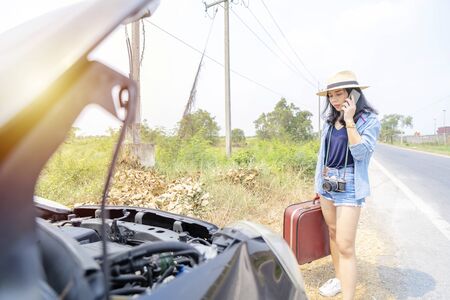 Cute Asian woman. She is using a smartphone to call for help. She traveled and experienced car intelligence until she had to ask for help.の写真素材