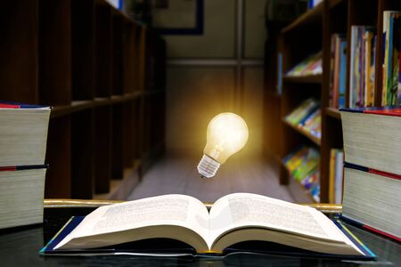 The open book was placed on a table in the library and there was a light bulb floating in the middle of the book. learning never ends concept.の写真素材