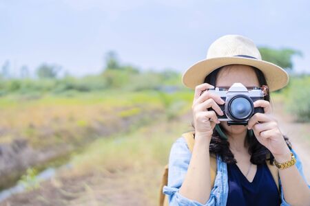 Photographer Asian covering her face with the camera. Portrait of a cute, cheerful girl with astonishing black hair, placing an outdoor camera, a woman resting in the gardenの写真素材