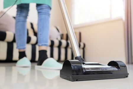 The housekeeper is cleaning the house with her vacuuming using a modern vacuum cleaner.の写真素材