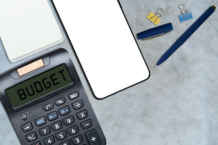 Budget planing concept. Top view of Calculator with word Budget, cup of coffee, smartphone on polished cement floor. Write idea success solution concept. Vintage toned picture. Copy spaceの写真素材