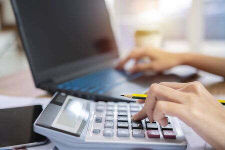 Woman accountant, office worker or bank worker uses calculator to calculate business profit and loss account. She presses number 5 on the calculator. Horizontal web banner style.の写真素材