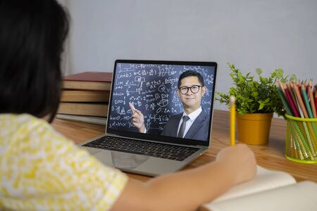 An Asian schoolgirl is studying homework math during her online lesson at home, social distance...