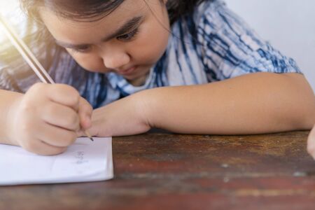 Asian children are studying exercises with determination. She uses a pencil to write on study materials.の写真素材
