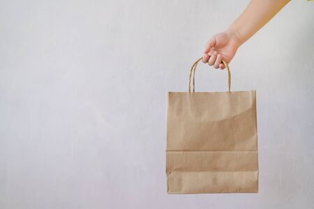 Asian girl is holding brown paper bag for mockup blank template. The background is a gray wall.の写真素材