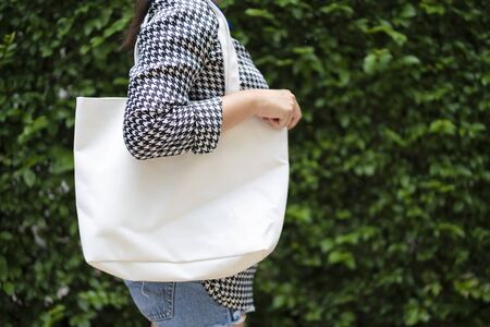 Asian girl is holding tote bag canvas fabric for mockup blank template. The background is a tree wall.の写真素材