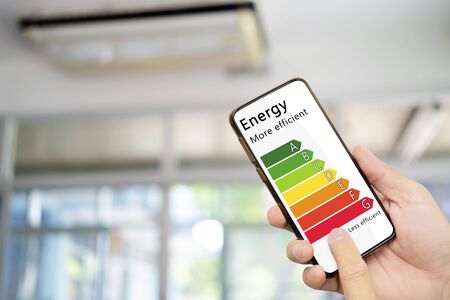 Hand holding digital smartphone and looking at house efficiency rating. Detail of house efficiency rating on digital tablet screen. Concept of ecological and bio energetic house. Energy class.の写真素材