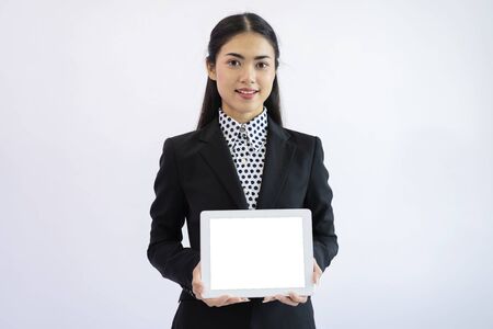 Portrait of an Asian businesswoman wearing a black suit. Hold an empty tablet to put text, images. Gray isolated backgroundの写真素材