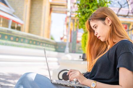 Shot of young asian female student sitting on a bench using a laptop, a female student studying in a...