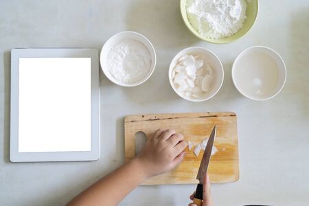 Top view, Children are using knives to cut raw materials in preparation for baking. With a tablet on the side, An Asian girl is learning to cook.の写真素材