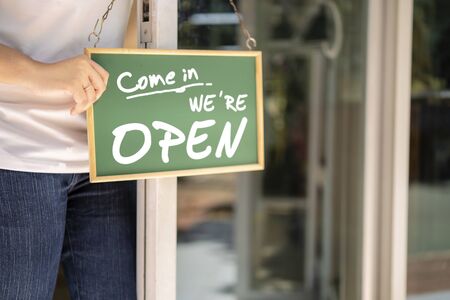 "Come in WE'RE Open" on cafe or restaurant hang on door at entrance. Asian restaurant owners are hanging a blackboard with the word welcome open to open the shop.の写真素材