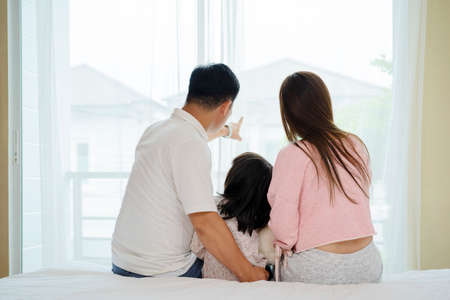 A happy Asian family, parents, daughter together Sitting on the bed looking out the windowの写真素材