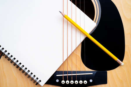 Acoustic guitar on white background, The guitar body pattern is wood grain. Notebook and yellow wooden pencilの写真素材