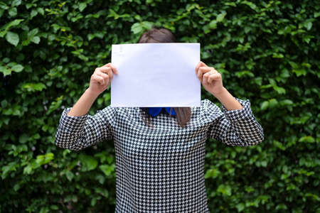An Asian woman is standing with a white paper over her face. Able to put text for advertising mediaの写真素材