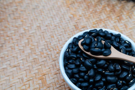 Black beans in a wooden spoon with a white ceramic bowl, placed on a wooden tray.の写真素材