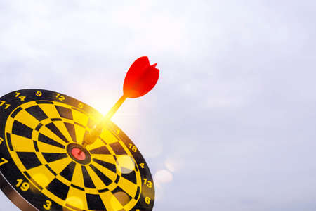 Red dart arrow hit in the target center of dartboard with sky backgroundの写真素材