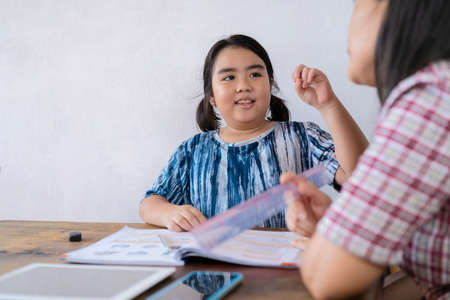A cute Asian female student studying closely with her teacher, She is telling the teacher a question.の写真素材