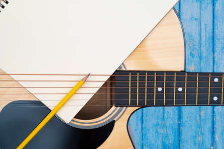 Acoustic guitar on blue background, The guitar body pattern is wood grain. Notebook and yellow wooden pencilの写真素材