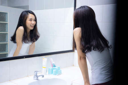 An Asian woman smiling to herself in front of a mirror in the bathroom, a bright new morning.の写真素材