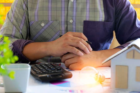Businessmen overlap their hands and light bulb nearby with using calculator to calculate and money stack. idea saving energy and accounting finance in office conceptの写真素材