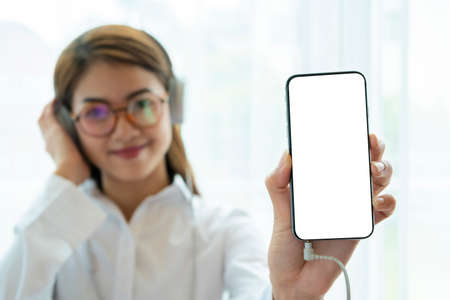 Beautiful Asian women listening to music with headphones and smartphones. A blank, white screen to enter ad text.の写真素材