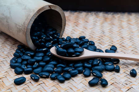 Black beans in a wooden spoon with a white ceramic bowl, placed on a wooden tray.