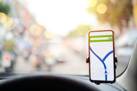 The map on the phone in the background of the dashboard. Black mobile phone with map gps navigation fixed in the mounting.の写真素材