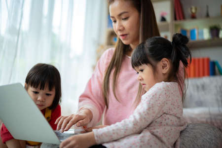 Loving mother resting relaxing with little preschool daughter and son together spend free time on weekend have fun using computer. Family surfing internet watch cartoons funny videos making video callの写真素材