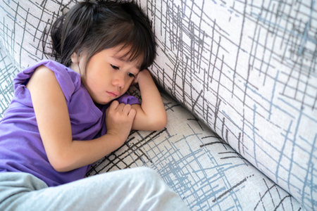 Distracted sad Asian girl looks out on the sofa in the living room at home. think of grief feel desperate sit aloneの写真素材