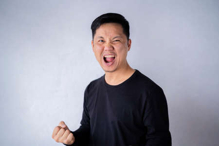 Happy winner. Happy young handsome man gesturing and keeping mouth open while standing against the cement wall.の写真素材