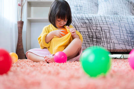 A cute Asian girl is happily playing colorful multicolor ballistic ball in the living room at home, putting the ball into her shirt.の写真素材