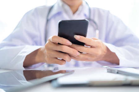 Female doctor hands holding and using mobile smart phone with laptop computer and stethoscope on the...
