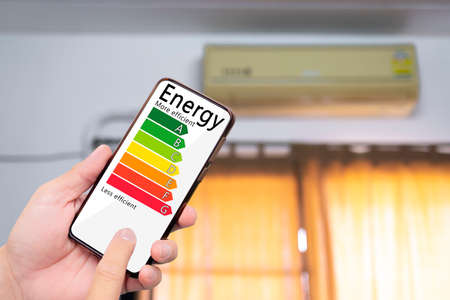 Hand holding digital smart phone and looking at house efficiency rating. Detail of house efficiency rating on digital tablet screen. Concept of ecological and bio energetic house. Energy class.の写真素材