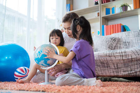 pretty family homeschooling mother happy teaching smart daughter private lessons in globe. asia seriously girl children touch map and curious watching.の写真素材