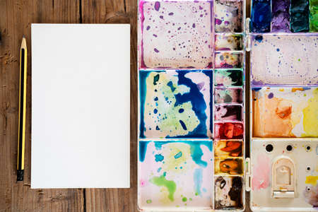 The palette water paints on the table, many color in the palette water paints. A blank drawing paper and a pencil are placed on the side.の写真素材