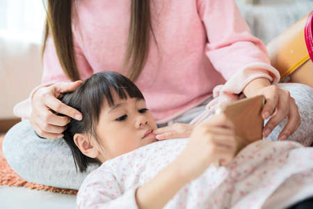 A beautiful mother and a young daughter are using smartphones and smiling while sitting on the...
